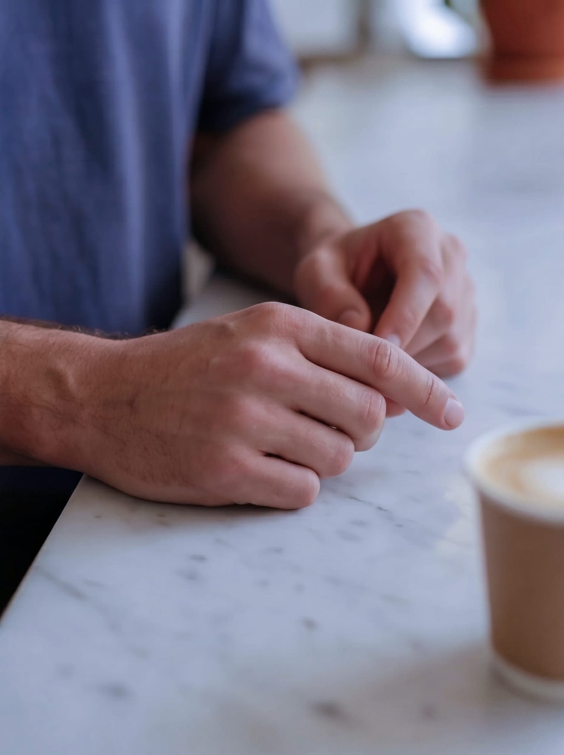 365.APParel Basic T-shirt Graphite — man, close-up of hands on marble counter, coffee cup nearby, café interior, indoor