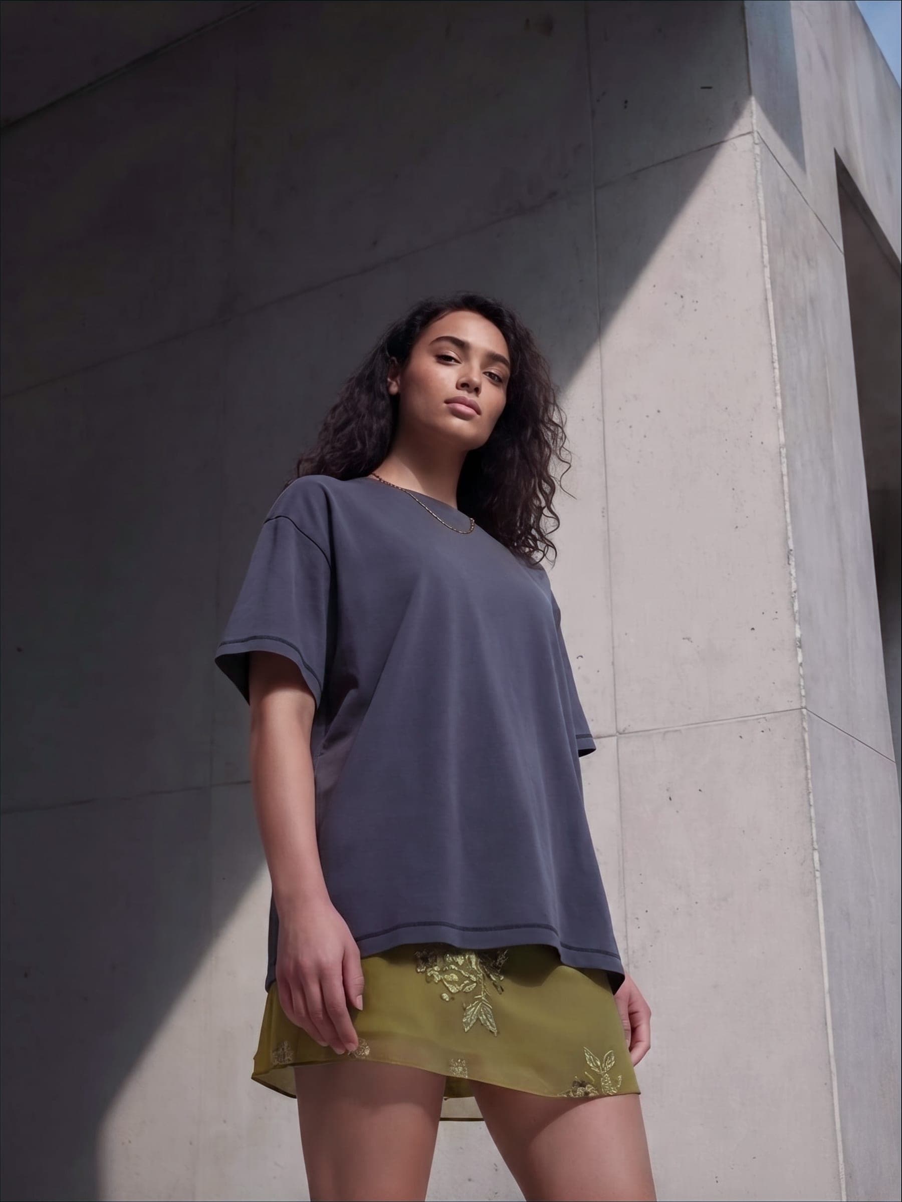 365.APParel Basic T-shirt Graphite — woman, three-quarter front view, looking down, concrete wall, outdoor