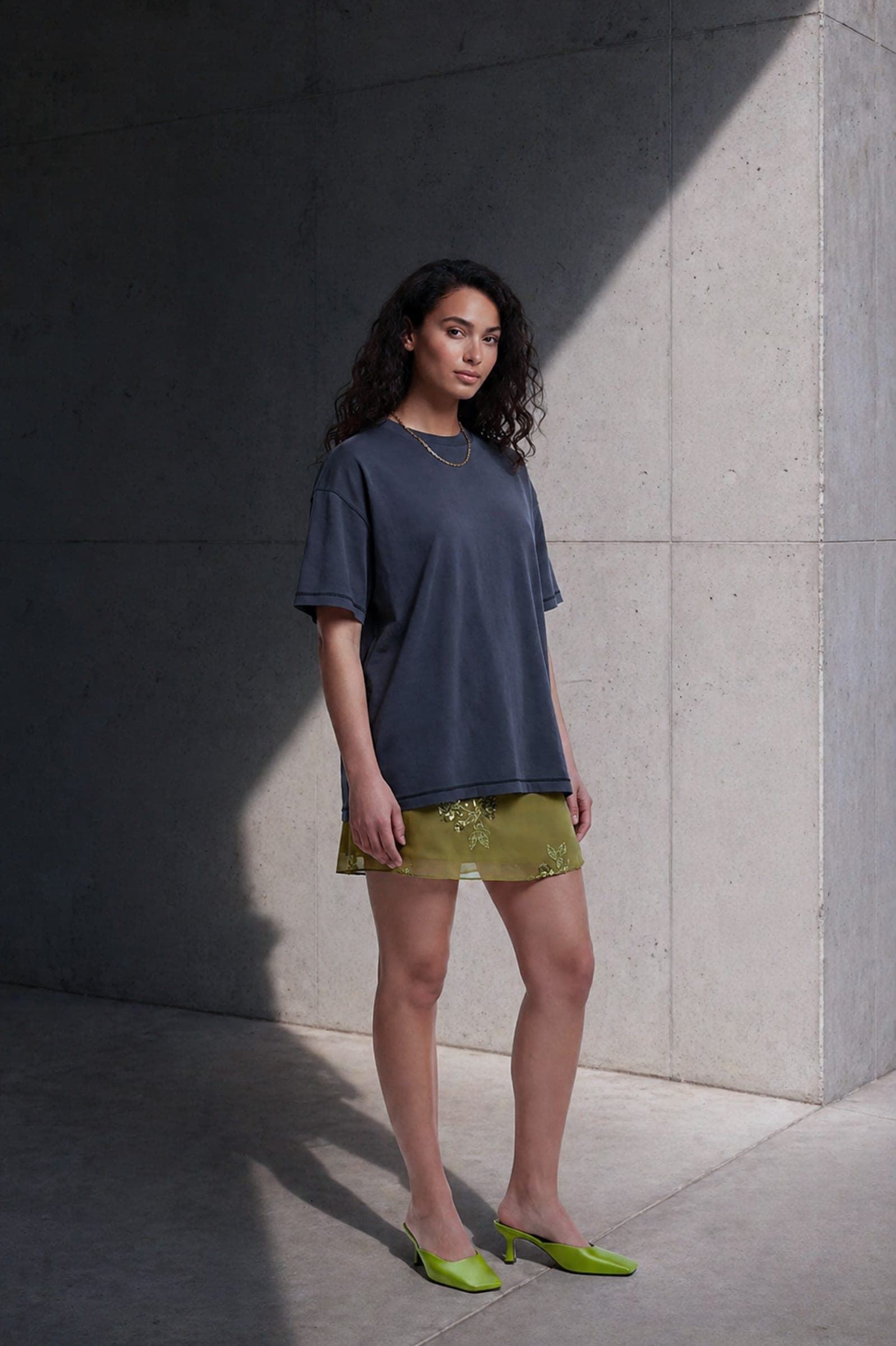 365.APParel Basic T-shirt Graphite — woman, full body, three-quarter side view, concrete wall, outdoor