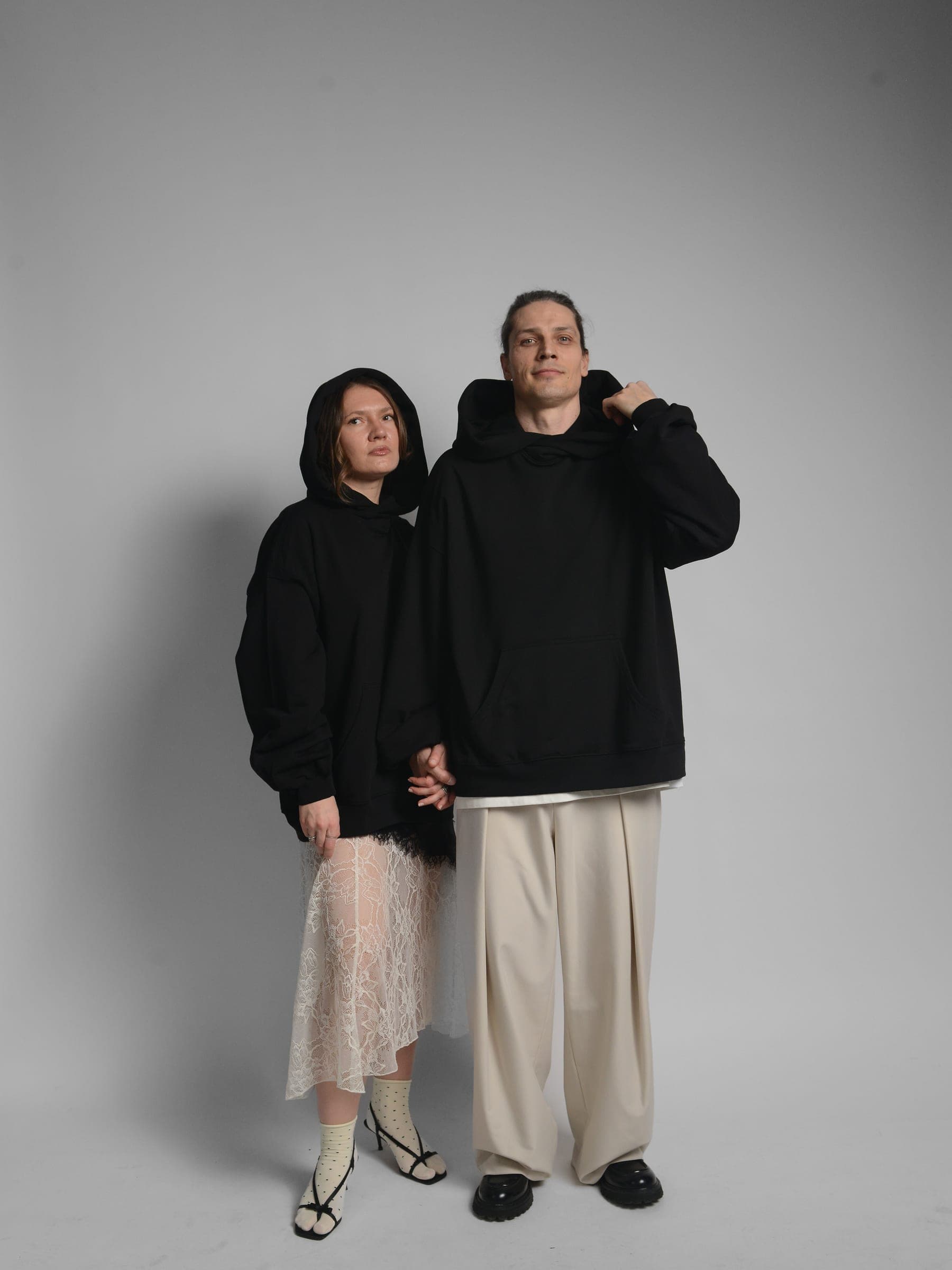 365.APParel Oversize Hoodie Black — couple in matching hoodies, front view, woman with lace skirt looking up, hood visible, studio
