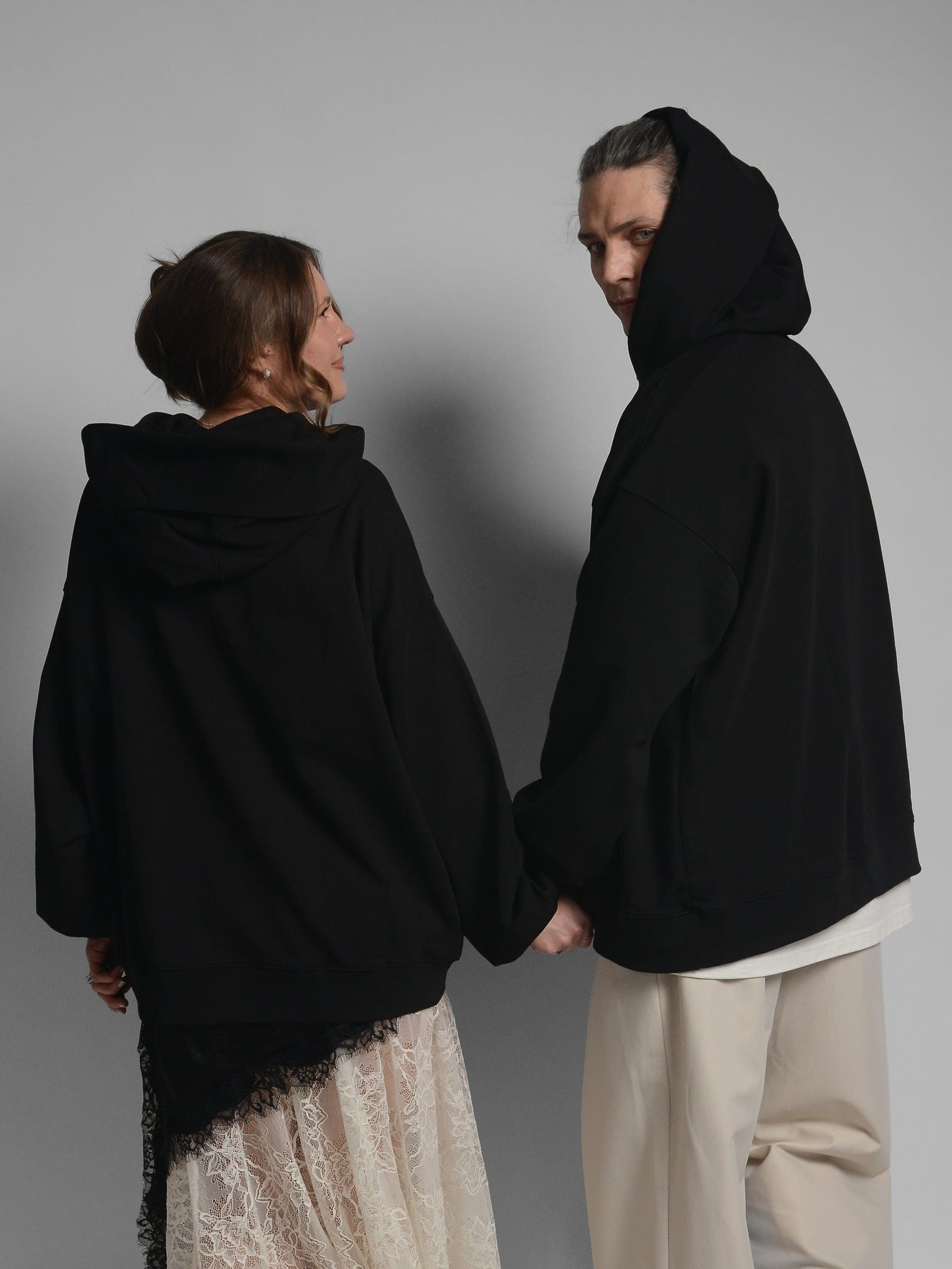 365.APParel Oversize Hoodie Black — couple in matching hoodies, three-quarter view, facing each other, hood visible, studio