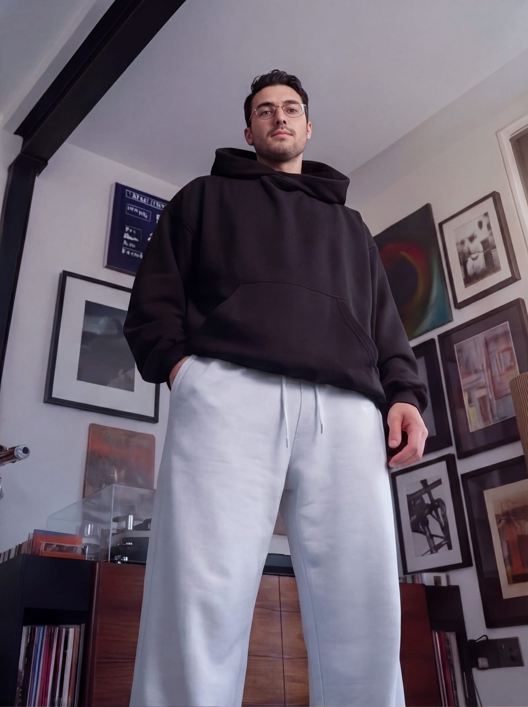 365.APParel Oversize Hoodie Black — man, cropped front view, hair in bun, slight smile, hood visible, cream wide-leg trousers, studio