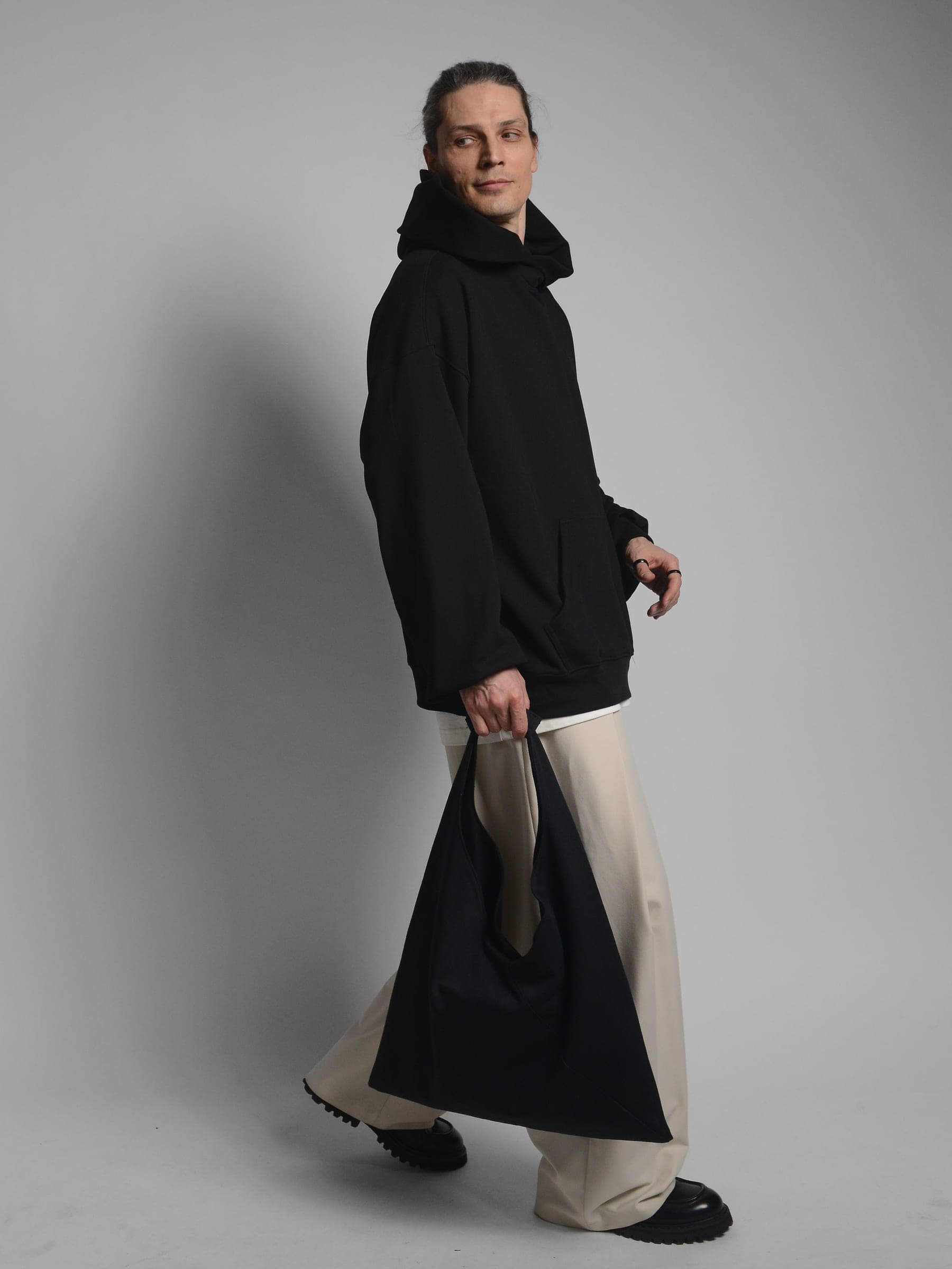 365.APParel Oversize Hoodie Black — man, full body front, glasses, hood visible, hands in pocket, home interior, indoor