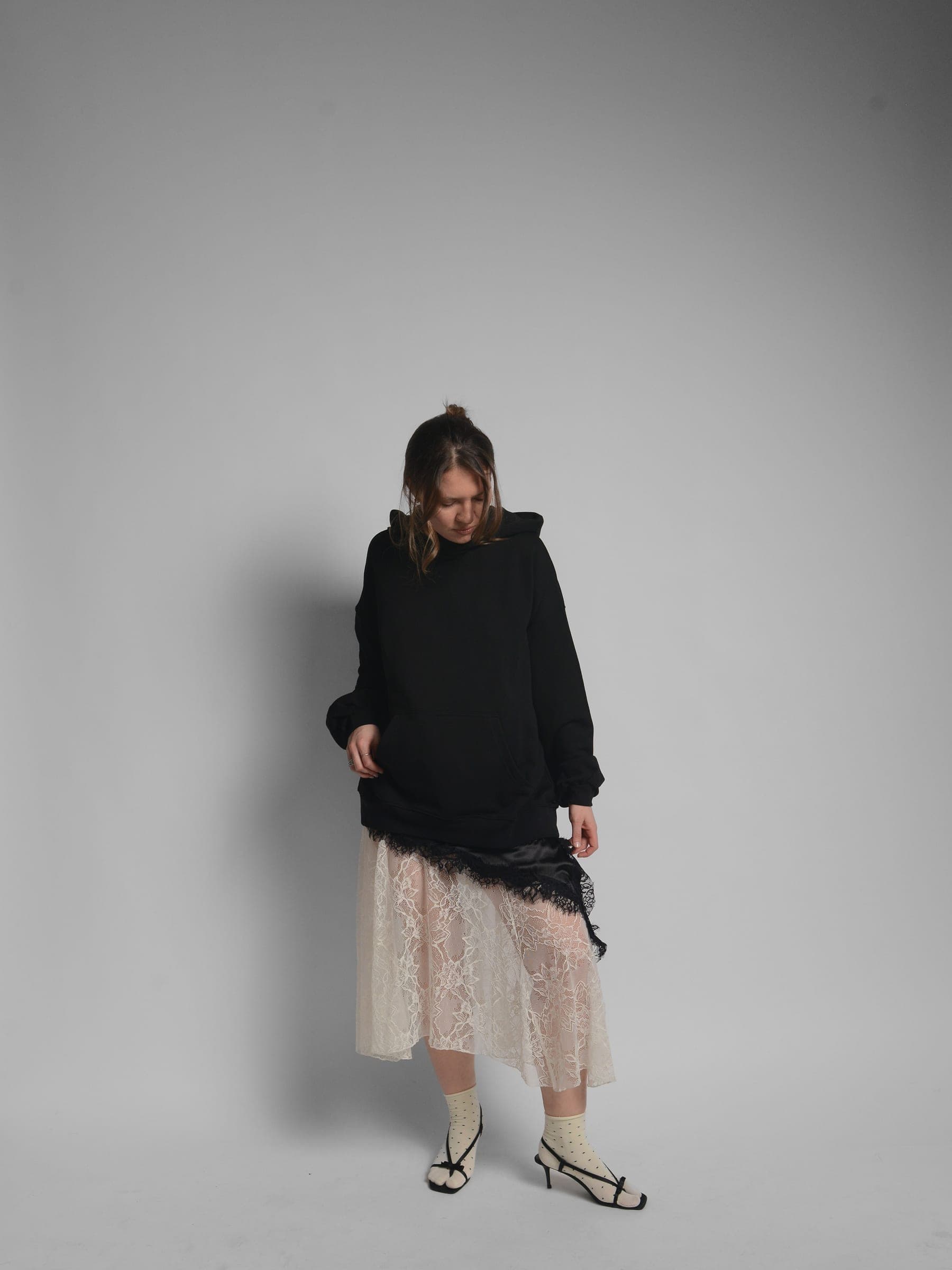 365.APParel Oversize Hoodie Black — woman, full body, head down, lace midi skirt, heeled sandals, hood visible, studio