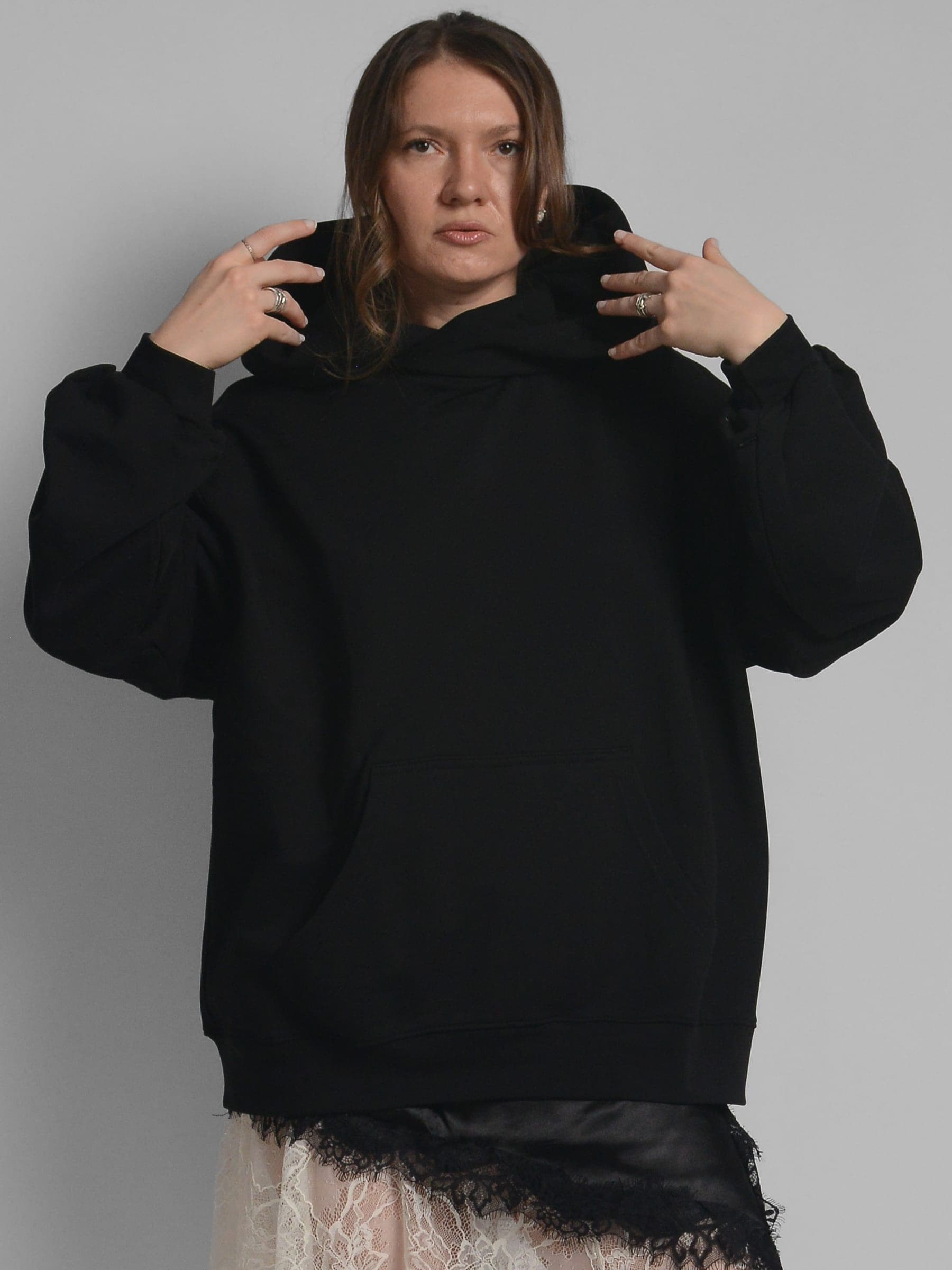 365.APParel Oversize Hoodie Black — woman, cropped front, pulling up hood with both hands, lace skirt, studio