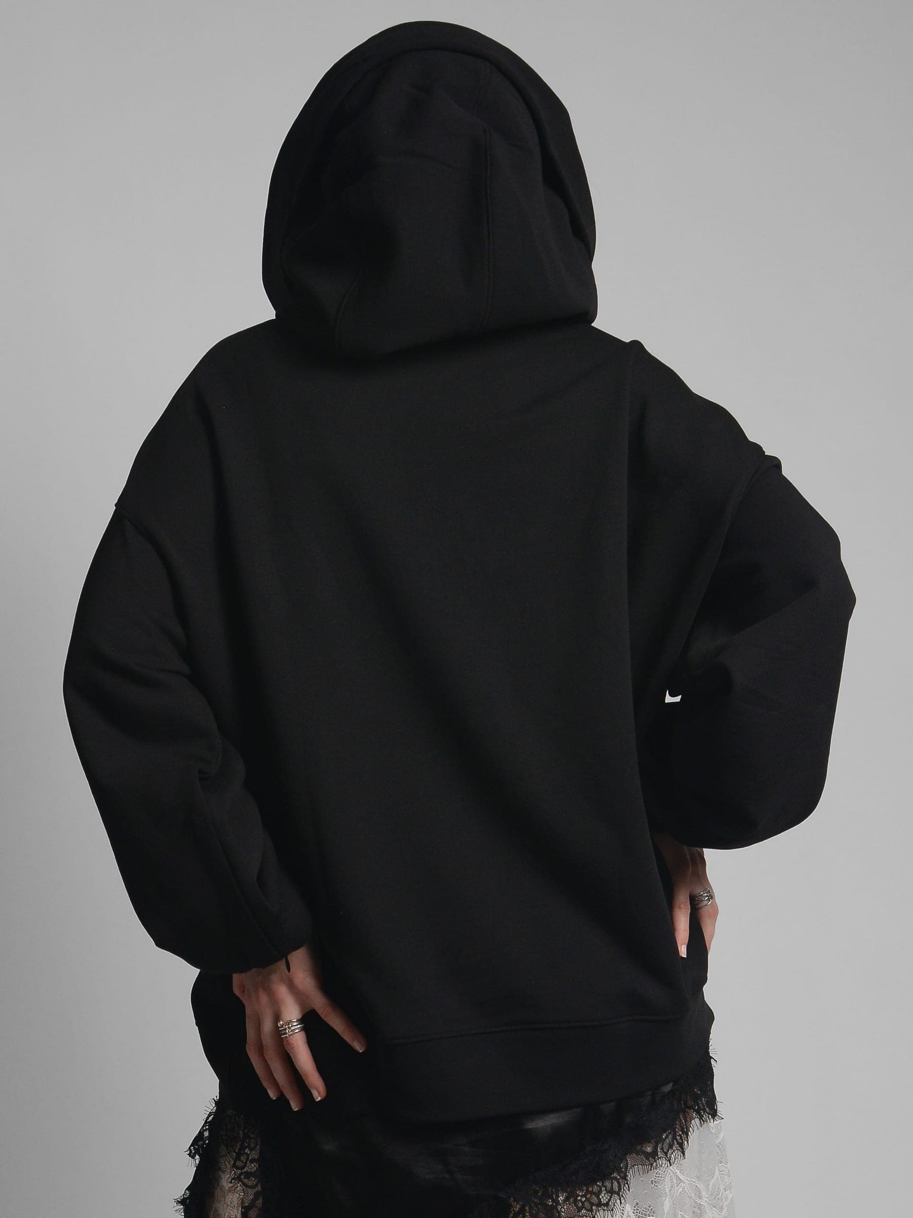 365.APParel Oversize Hoodie Black — woman, cropped back view, hood up, hands on hips, lace skirt visible, studio