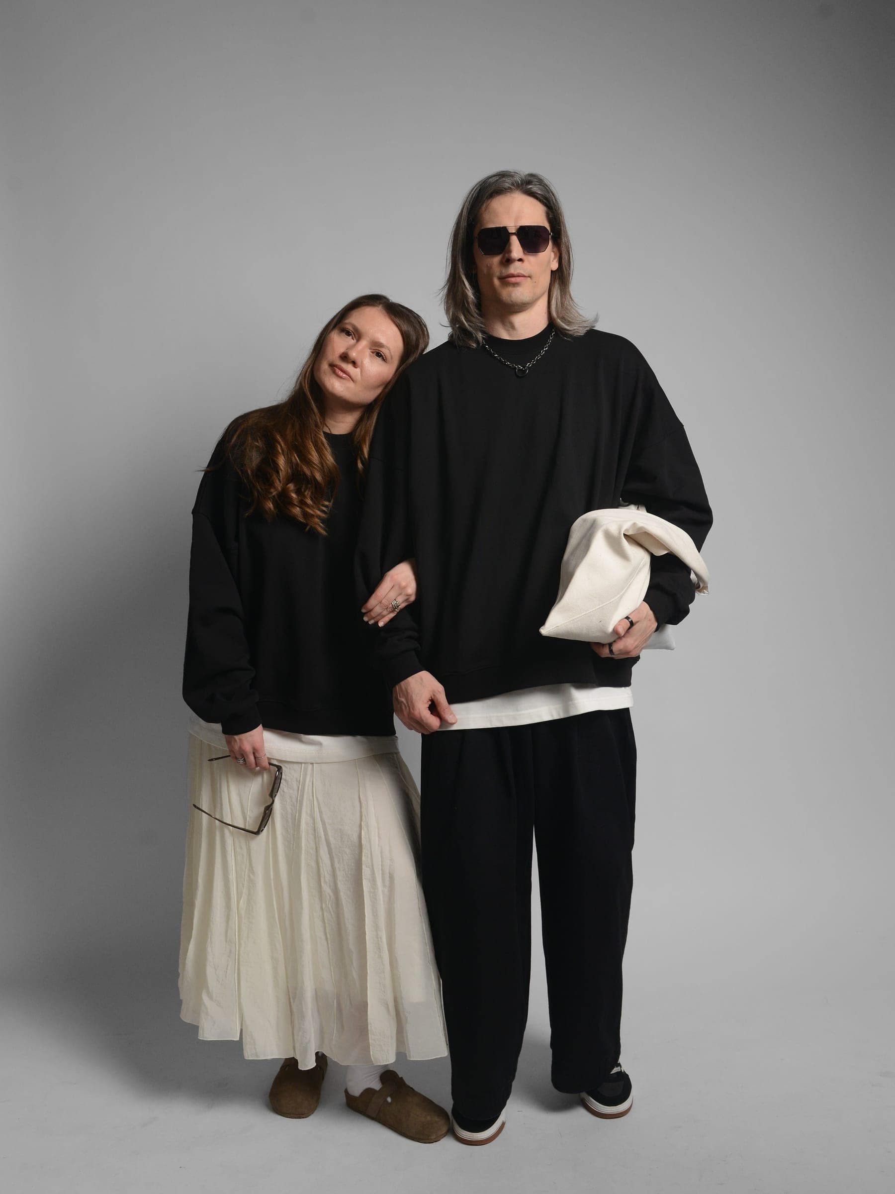 365.APParel Oversize Sweatshirt Black — couple, full body front, woman leaning on man, man holding tote bag, sunglasses, studio