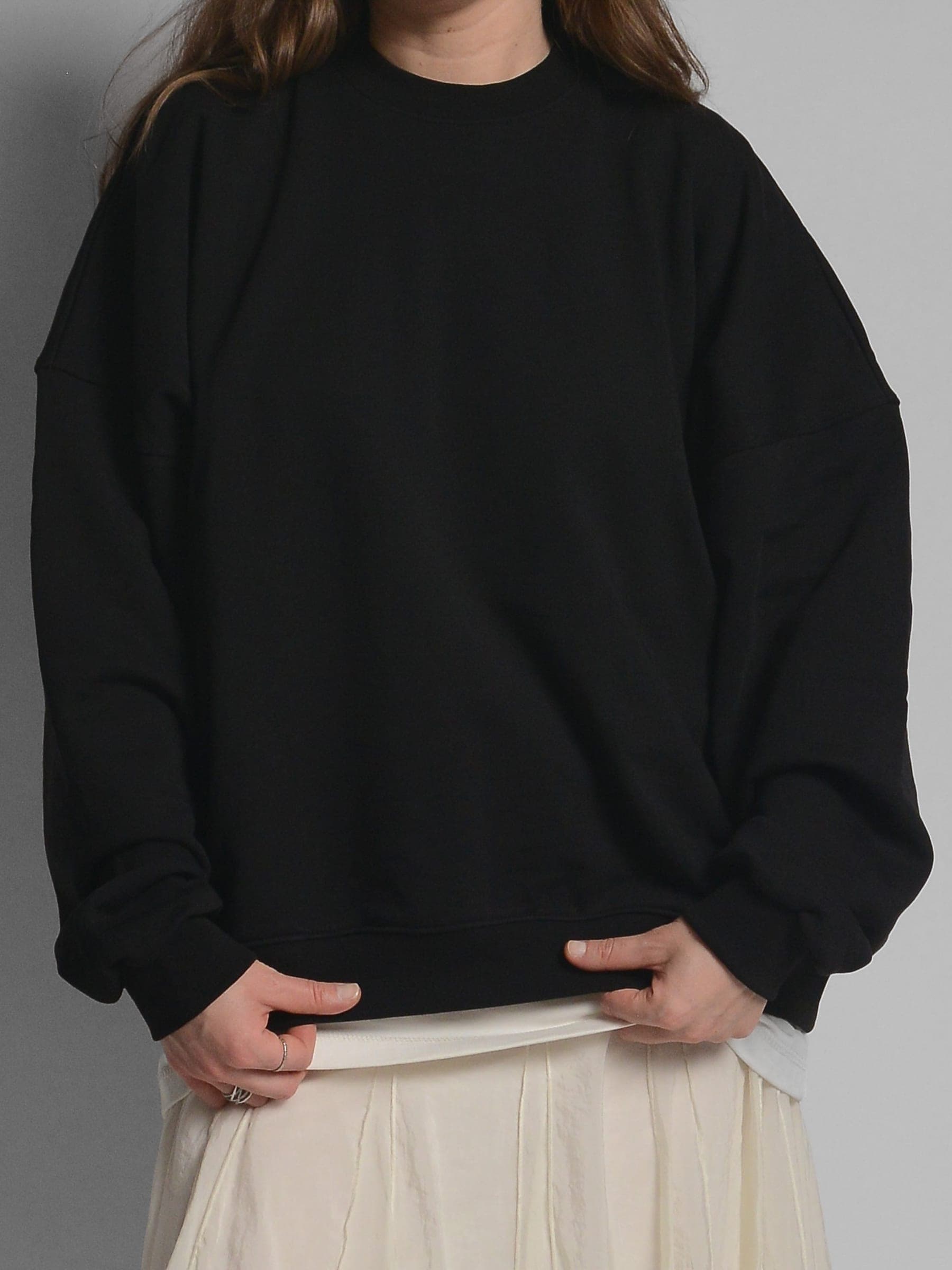 365.APParel Oversize Sweatshirt Black — woman, cropped front view, lifting hem, pleated skirt underneath, studio