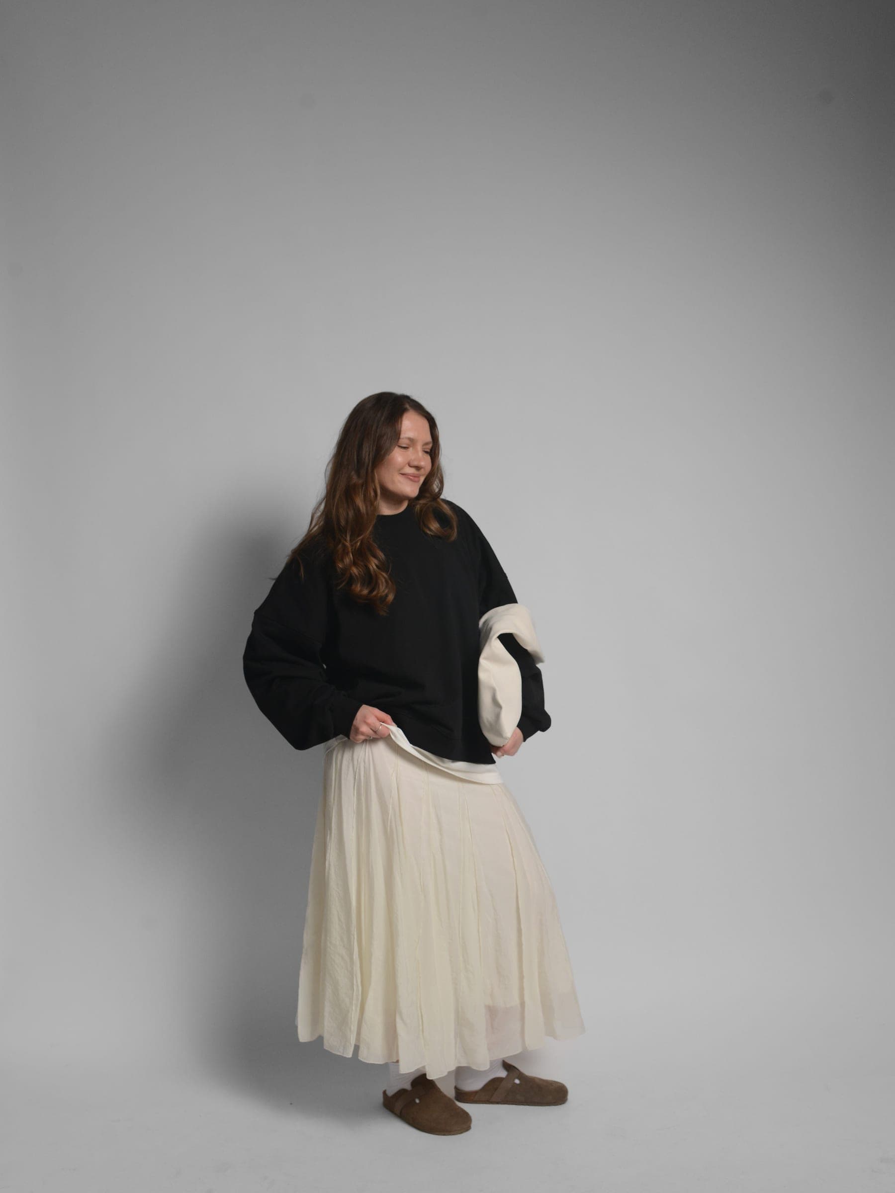 365.APParel Oversize Sweatshirt Black — woman, full body three-quarter view, smiling, tote bag, pleated maxi skirt, studio
