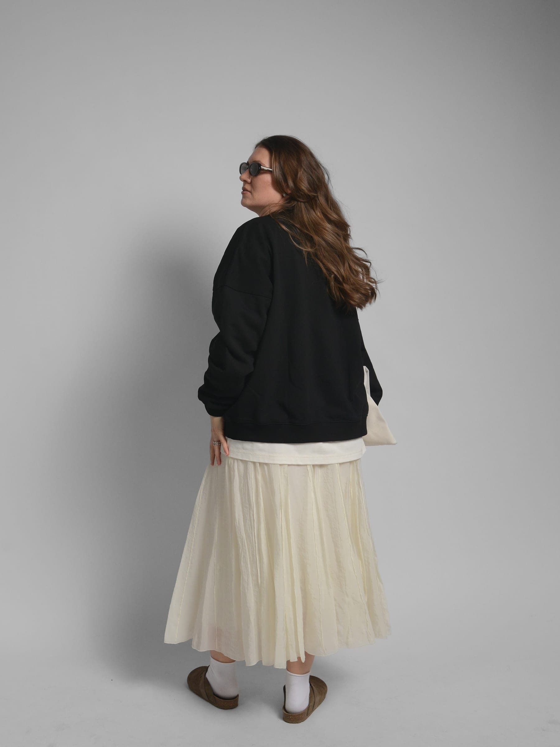 365.APParel Oversize Sweatshirt Black — woman, full body three-quarter back view, sunglasses, tote bag, pleated maxi skirt, studio