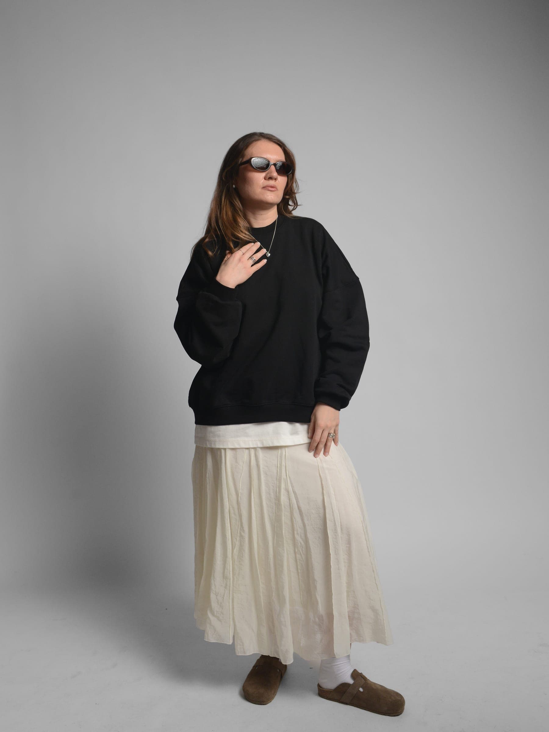 365.APParel Oversize Sweatshirt Black — woman, full body three-quarter front view, sunglasses, hand on chest, pleated maxi skirt, studio