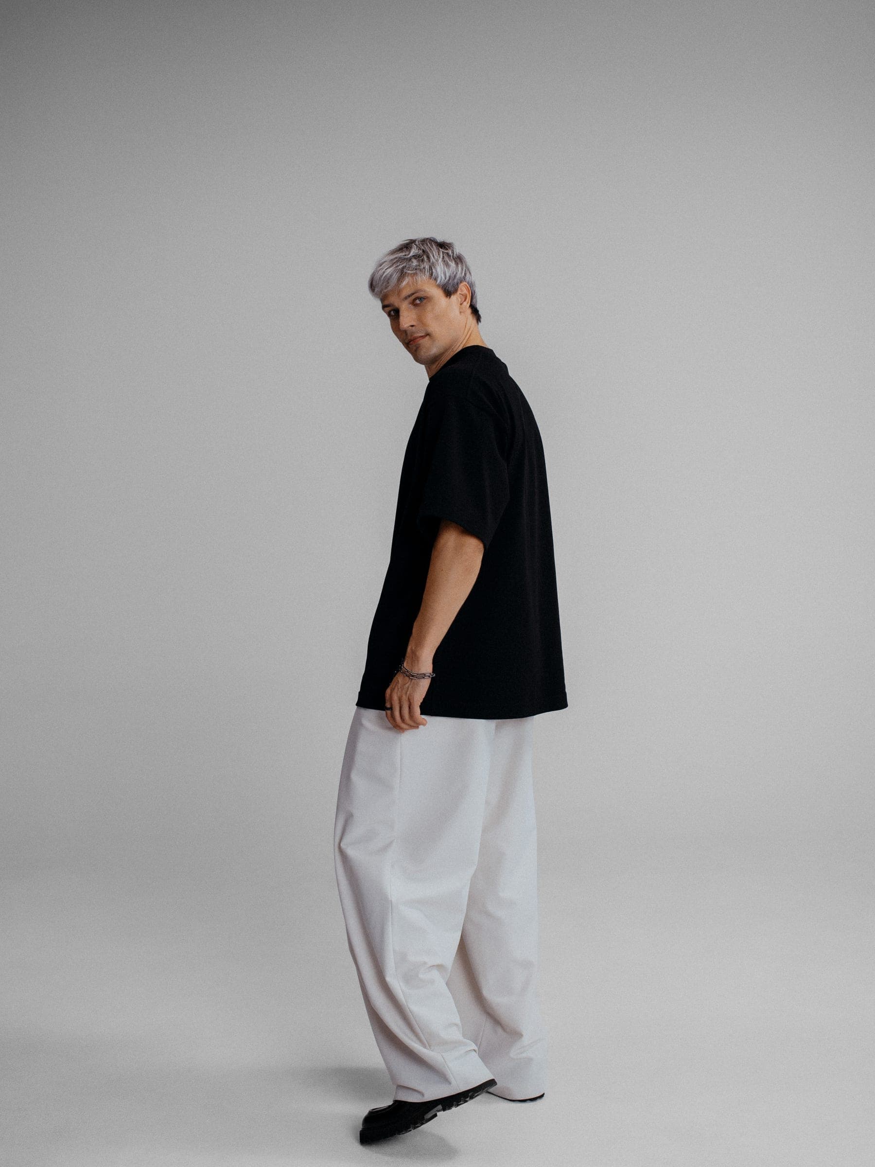365.APParel Oversize T-shirt Black — man, full body side view, gray hair, looking back, white trousers, studio