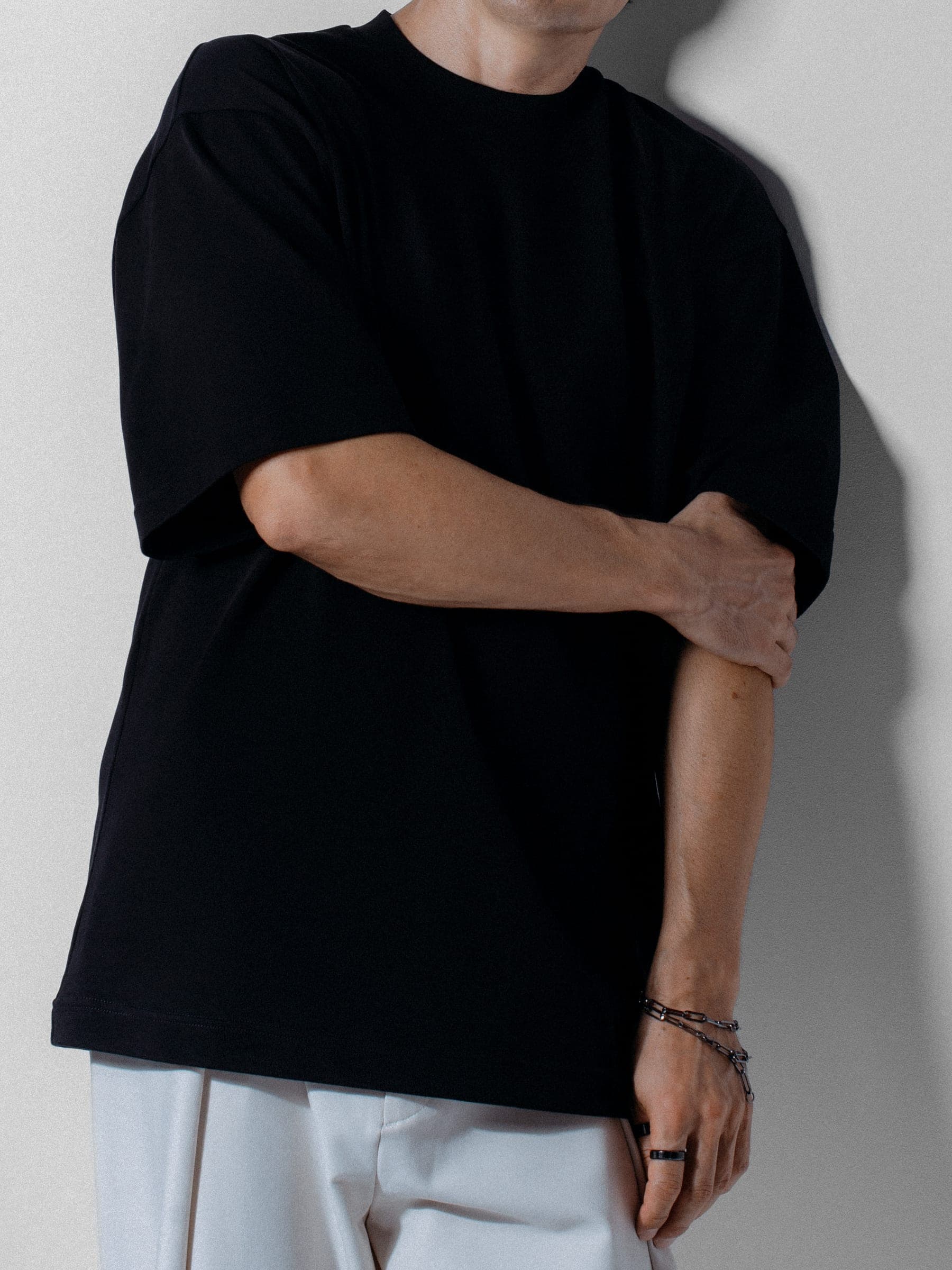 365.APParel Oversize T-shirt Black — man, cropped front view, arms crossed, chain bracelet, white trousers, studio